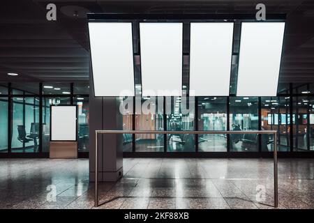 Vier vertikal orientierte leere Mock-ups von tv-Bildschirmen einer Abflug- und Anfahrtafel und eine Vorlage einer indoor Werbeplakatwand entfernt in der Nähe eines Glases w Stockfoto