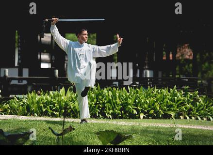 Junger Mann praktiziert traditionelles Tai Chi Schwert, Tai Ji im Park für gesunde, traditionelle chinesische Kampfkunst Konzept auf natürlichem Hintergrund . Stockfoto