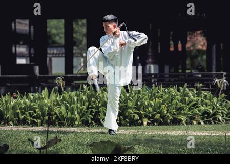 Junger Mann praktiziert traditionelles Tai Chi Schwert, Tai Ji im Park für gesunde, traditionelle chinesische Kampfkunst Konzept auf natürlichem Hintergrund . Stockfoto