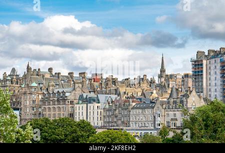 Wunderschöne Gebäude und Dächer von Edinburgh New Town, von den Princes Street Gardens aus gesehen, grüne Sommerbäume im Vordergrund, blauer Himmel, flauschige weiße Wolken, Stockfoto