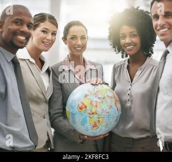Bereit, die Welt zu übernehmen. Beschnittenes Porträt einer Geschäftsfrau, die einen Globus hält, während sie mit ihren Kollegen steht. Stockfoto