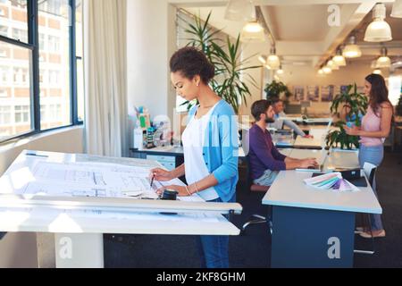 Shes eine ausgezeichnete Architektin. Eine junge Architektin, die an ihrem Entwurfstisch arbeitet. Stockfoto