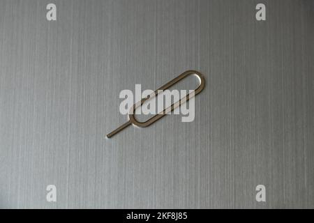 Der Clip zum Öffnen eines Steckplatzes für eine SIM-Karte liegt auf einem grauen Stahl Stockfoto