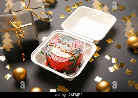 Lunchbox aus Kunststoff mit leckeren Bento-Kuchen, Geschenken und Weihnachtsdekorationen auf dunklem Hintergrund Stockfoto