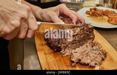 Der Koch schneidet Scheiben aus einem Stück lang gegartem Rindfleisch Stockfoto