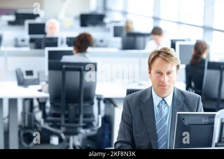 Jahrelange Erfahrung nutzen. Reifer Geschäftsmann sitzt auf einem Computer im Büro - Porträt. Stockfoto