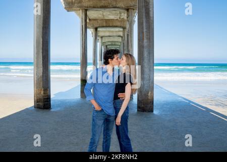 Junges Paar, das sich unter dem Scripps Pier, La Jolla, Kalifornien, küsst Stockfoto