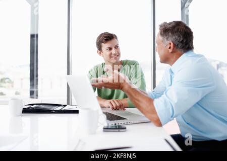 Von den Besten lernen. Ein reifer Manager schaut sich mit einem jüngeren Kollegen die Arbeit auf einem Laptop an. Stockfoto
