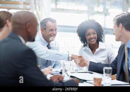 Ich denke, wir haben eine Vereinbarung. Zwei Geschäftsleute, die eine Einigung erzielen, während sie mit anderen Geschäftsleuten an einem Tisch sitzen. Stockfoto