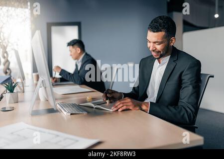 Afrikanischer Geschäftsmann, der sich während des Arbeitstages im Büro Notizen über den Hintergrund eines Kollegen gemacht hat Stockfoto