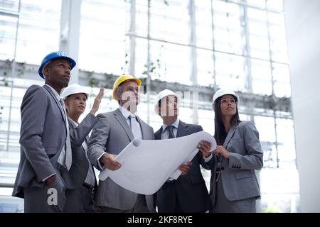 Vor-Ort-Inspektion... Eine Aufnahme aus dem niedrigen Winkel einer Gruppe von Architekten, die mit Blaupausen nach oben schauen. Stockfoto
