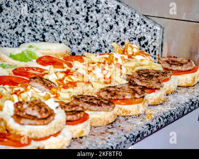 Burger in einer Reihe auf der Arbeitsplatte, Fokus auf offene Hamburger gefüllt mit pommes frites, Salat und Tomaten, gegrillte gehackte Steaks, Mayonnaise und Ketchup. Stockfoto