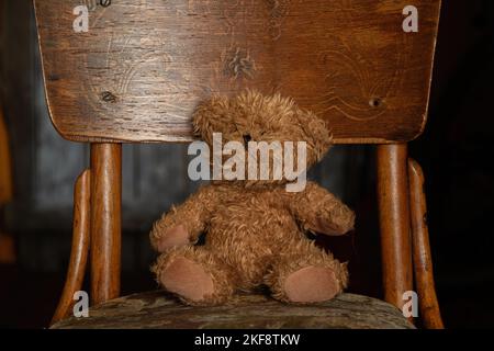 teddybär sitzt auf einem alten weichen Stuhl im Dunkeln im Zimmer zu Hause, Kinderspielzeug, Teddybär Stockfoto