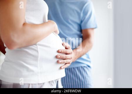 Große Erwartungen. Seitenansicht einer Schwangeren, die ihren Bauch hält, während der Ehemann ihn in Zuneigung berührt. Stockfoto