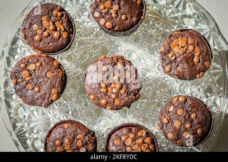 Blick von oben auf hausgemachte Muffins mit Schokoladenkuchen auf einer Glasplatte. Direkt über der Nahaufnahme Makrofotografie mit seitlicher Sonneneinstrahlung. Stockfoto