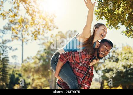 Vielfältig, Paar und Huckepack Spaß mit einem Mann und einer Frau Spaß in der Natur im Sommer. Abenteuer, glückliches Paar und interracial Menschen in einem Grün Stockfoto