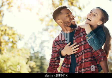 Pärchen, umarmen und lächeln Sie im Freien mit Liebe und Sorgfalt in der Natur, glücklich zusammen, während Sie sich im Park verbinden. Schwarzer Mann, Frau und interracial, umarmt in Stockfoto