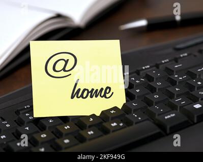 Gelbe Notiz mit At-Schild und Text, zu Hause, auf einer schwarzen Tastatur am Schreibtisch zu Hause, Konzept für das Home Office oder flexible Arbeitszeiten von zu Hause aus Stockfoto