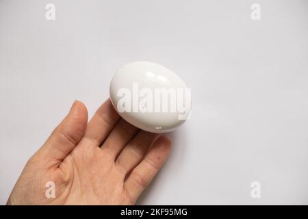 Etui mit kabellosen Kopfhörern in Form eines Ovals liegt in der Hand des Mädchens auf einem isolierten Hintergrund, kabellose Kopfhörer, Musik, Ladetasche für Stockfoto