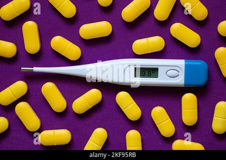 Elektronisches Thermometer liegt neben gelben Pillen auf einem isolierten Hintergrund, Medizin und Apotheke, Gesundheit und Behandlung, Pillen und Antibiotika Stockfoto