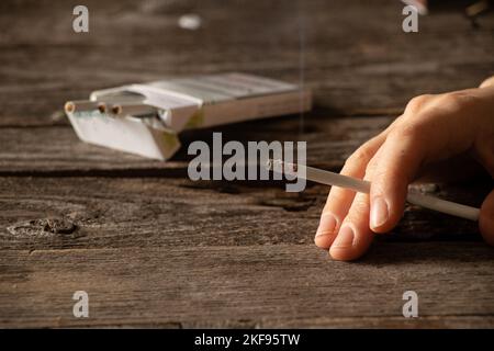 Frau, die eine Zigarette zu Hause am Tisch hält, im Dunkeln zu Hause raucht, Nikotin und schlechte Angewohnheit, Zigaretten und Krebs und Rauchen Stockfoto