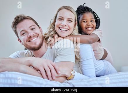 Familie, Eltern und Kind im interracial Portrait auf dem Bett mit Lächeln, Liebe oder glücklicher Bindung zu Hause. Schlafzimmer, multikulturelle Vielfalt und Stockfoto