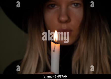 Ein Mädchen in einem schwarzen Hut im Dunkeln hält eine Kerze, ein Mädchen mit Kerzen in der Nacht Stockfoto