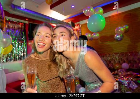 Zwei fröhliche weiße Freundinnen, die in einem Nachtclub Champagner trinken Stockfoto