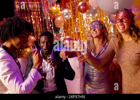 Vier fröhliche, vielfältige Freunde, die lachen und Champagner trinken auf einer Party in einem Nachtclub Stockfoto