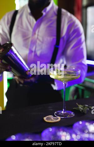 Vertikal vom Mittelteil des afroamerikanischen Barkeepers, der grünen Cocktail an einer Bar zubereitet, selektiver Fokus Stockfoto