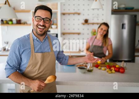 Das junge glückliche Paar genießt und bereitet gemeinsam gesunde Mahlzeiten in ihrer Küche zu Stockfoto