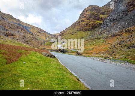 Menschen gehen zu Fuß und Autos fahren auf dem Honnister Pass, Lake District, Cumbria. Stockfoto