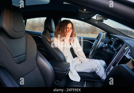 Müde Geschäftsfrau Gähnen während Auto selbst fahren in fortgeschrittenen Auto Fahrzeug, Caucaisan weibliche Besitzer haben Autopilot-Reise mit Freisprechmodus in autonomen Automobil Stockfoto