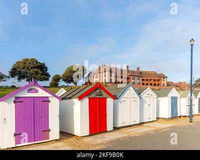 Bunte Strandhütten am Meer, Barlet Hospital Gebäude dahinter, Felixstowe, Suffolk, England, Großbritannien Stockfoto