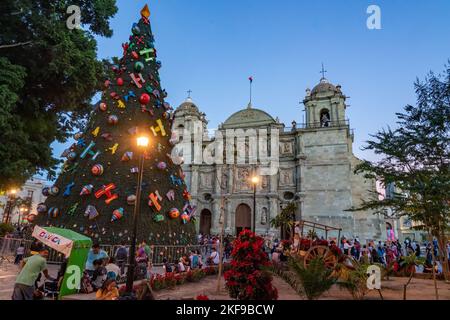 Ein Weihnachtsbaum vor der Kathedrale mit Menschenmassen, die zu Weihnachten auf dem Zocalo in der Stadt Oaxaca, Mexiko, feiern. Stockfoto