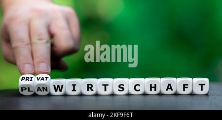 Die Hand dreht Würfel und ändert den deutschen Ausdruck "Planwirtschaft" in "Privatwirtschaft". Stockfoto
