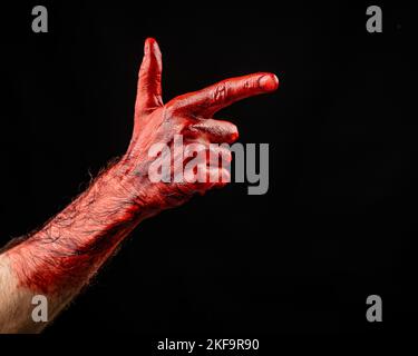 Blutige männliche Hand zeigt eine Waffe vor schwarzem Hintergrund. Stockfoto