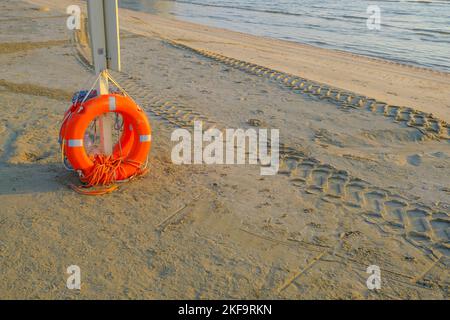 Orangefarbene Rettungsboje aus nächster Nähe am Strand entlang der Küste bei Sonnenaufgangslichtern. Sicherheit am Strand. Lebensretter Stockfoto