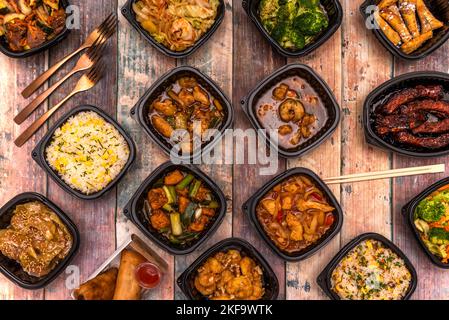 Set asiatischer Rezepte in schwarzen Lieferbehältern mit Essstäbchen und Kupferbesteck Stockfoto