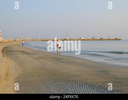 Juli 2022 Senigallia, Italien: Älterer Mann, der am Strand über das Meer, den Sonnenaufgang und den Horizont in Richtung Kamera geht Stockfoto