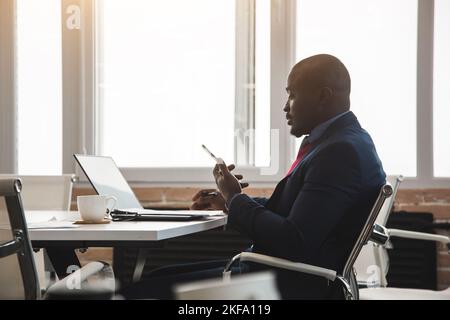 Porträt eines Afroamerikaners im Büro. Schwarzer Mann in einem Geschäftsanzug, der an einem Laptop arbeitet Stockfoto