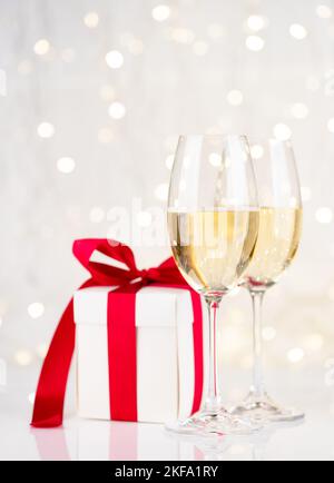 Sektgläser und Geschenkbox vor Weihnachtslichtern Bokeh Stockfoto