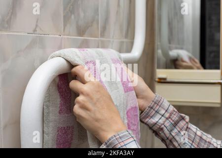 Frau hängt ein Handtuch auf einem beheizten Handtuchhalter. Mann trocknet Handtuch Stockfoto