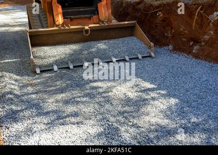 Der Bobcat-Lader-Bagger wurde auf der Baustelle zum Entladen von Schotter bei Straßenreparaturen eingesetzt. Stockfoto