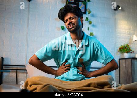 Junger Mann, der an Magenschmerzen oder Magenschmerzen leidet, während er nachts schläft - Konzept von Gesundheitsproblem, Lebensmittelvergiftung und ungesund Stockfoto