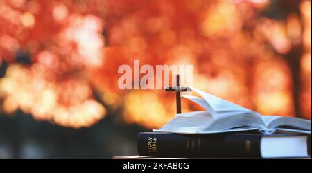 Rote Ahornblätter und Herbstbäume im Wald und das Heilige Kreuz Jesu Christi und bibelbuch auf dem Tisch Stockfoto