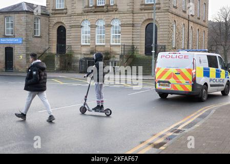 Junge auf Elektroroller überqueren die Straße mit der Polizei van vorbei. Stockfoto