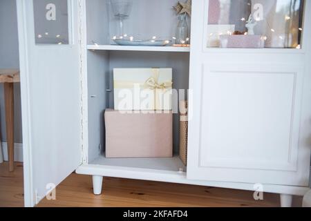 In einem weißen Anrichte aus Holz sind pinke Weihnachtsboxen mit einem goldenen Band gebunden. Eine helle Girlande sorgt für eine festliche Atmosphäre im Haus. Christma Stockfoto