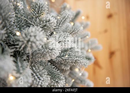 Draufsicht auf einen schneebedeckten, künstlichen Weihnachtsbaum mit hellen Girlanden, steht auf einem Holzlaminatboden. Urlaubskarte, minimalistischer Stil. Verschwommen Stockfoto