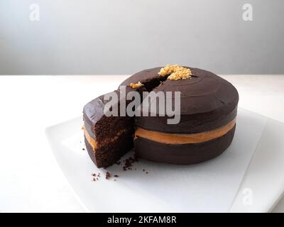 Schneiden Sie ein Stück veganen Schokoladenkuchen mit Erdnussbutter-Füllung, bedeckt mit Schokoladencreme auf weißem Hintergrund Stockfoto